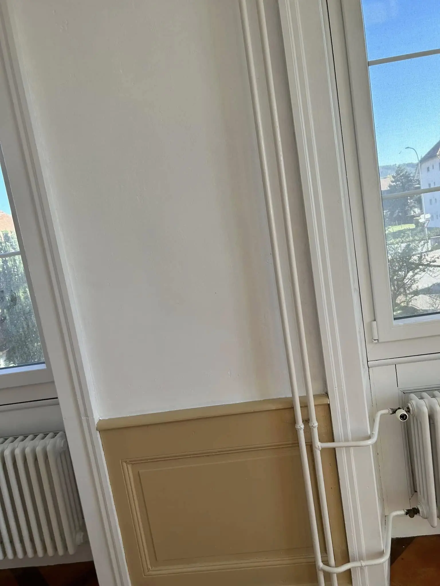 Conduites de chauffage repeintes en blanc le long du mur, soubassement repris en beige