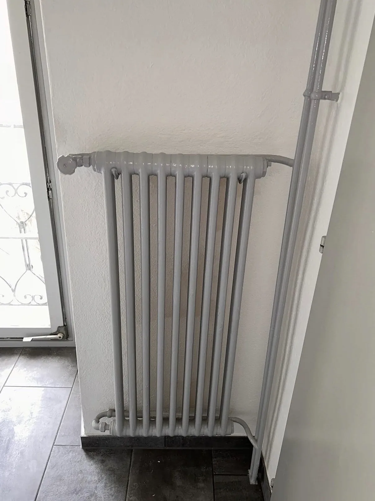 Radiateur et tuyaux repeints en gris clair, mur crépi blanc, à Estavayer-le-Lac