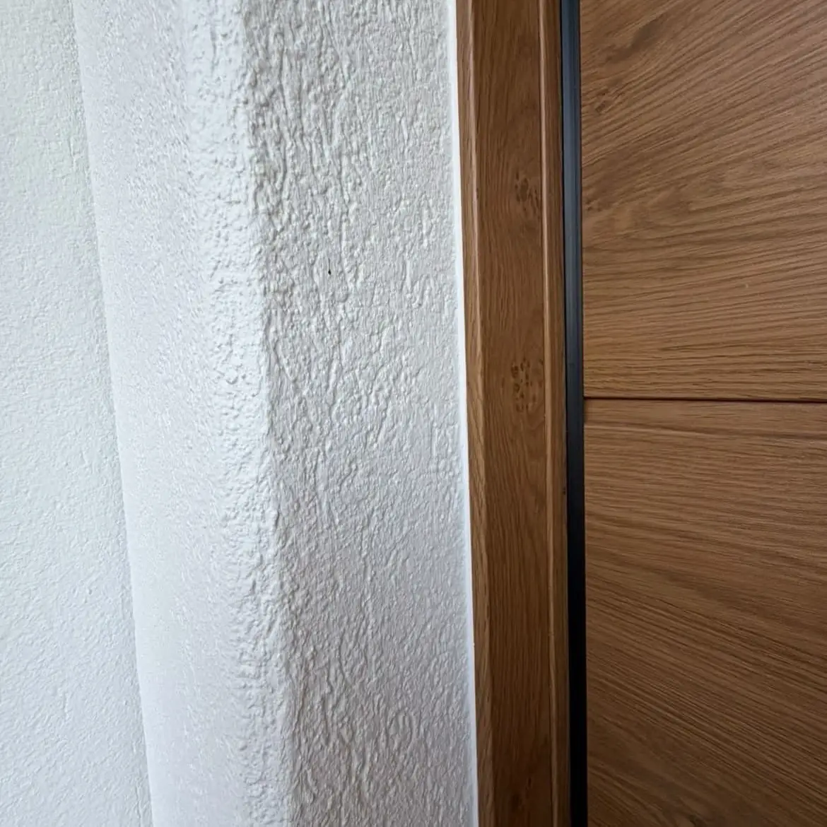 Arête du crépi repeinte en blanc le long de l'encadrement bois de la porte de garage
