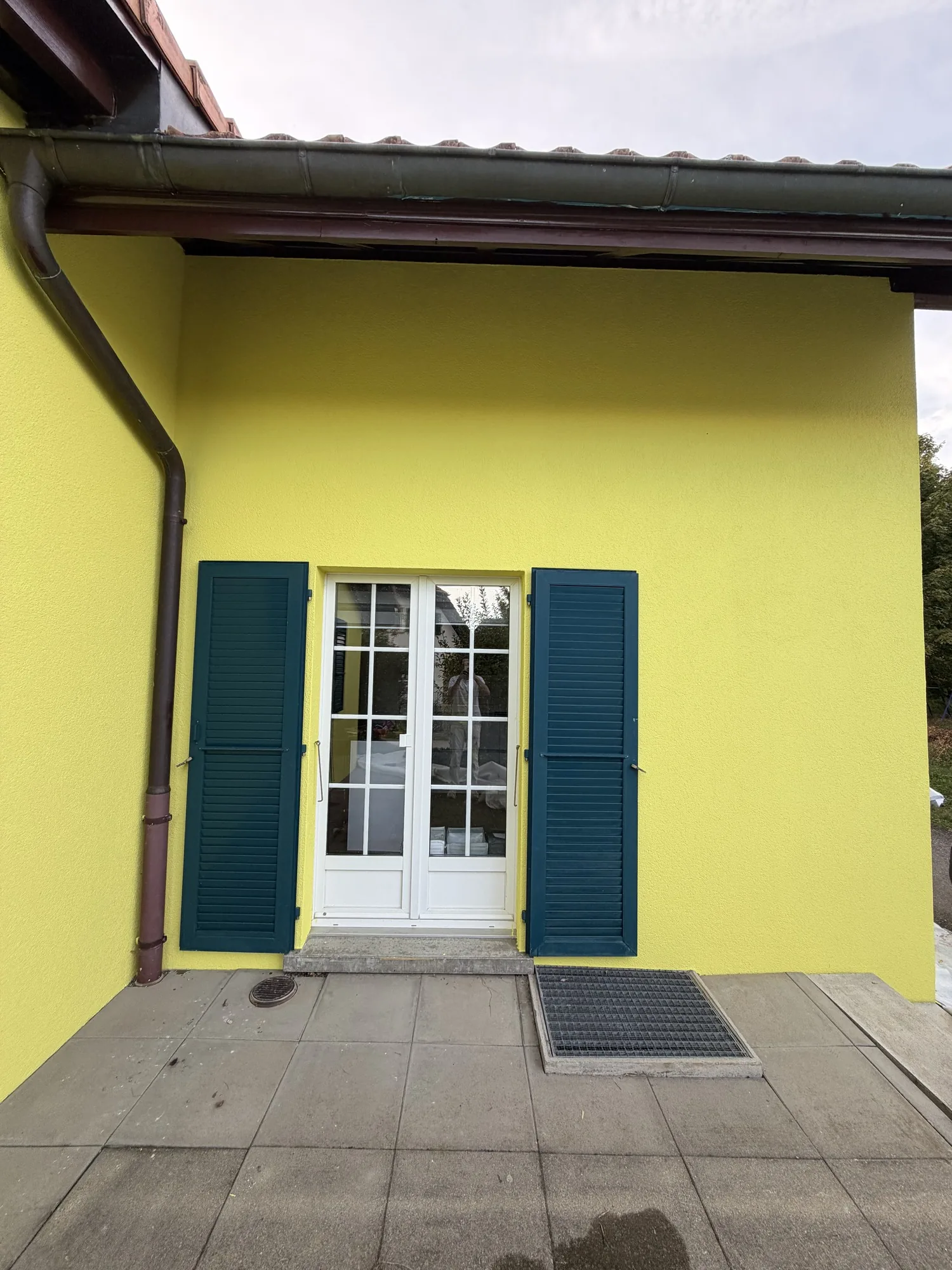 Volets laqués vert foncé autour d'une porte-fenêtre, façade jaune, à Billens