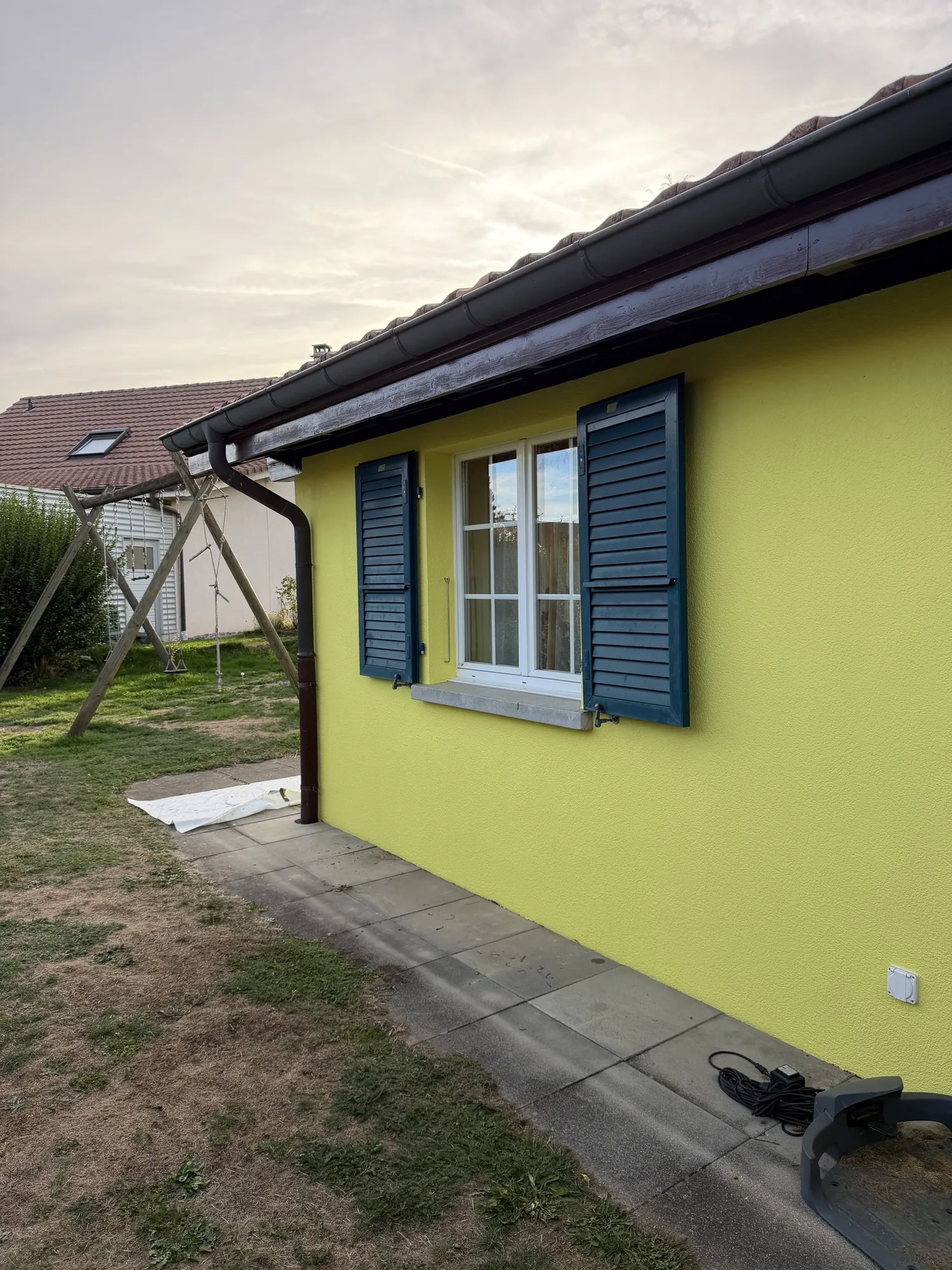 Pignon repeint en jaune, volets vert foncé, sous-face de toit brune, à Billens
