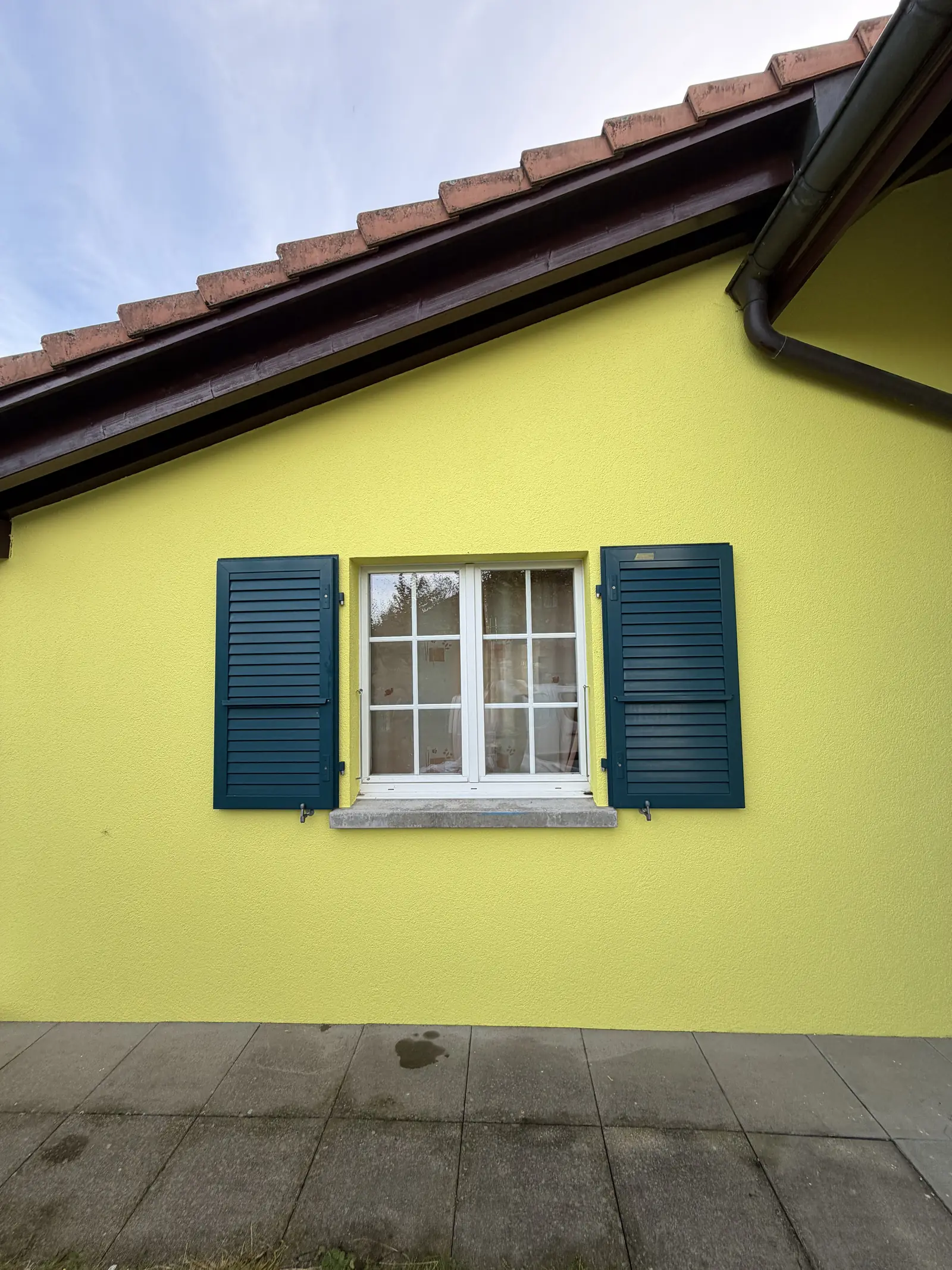 Façade terminée, crépi en jaune citron et avant-toit repeint en brun au-dessus des volets bleu pétrole