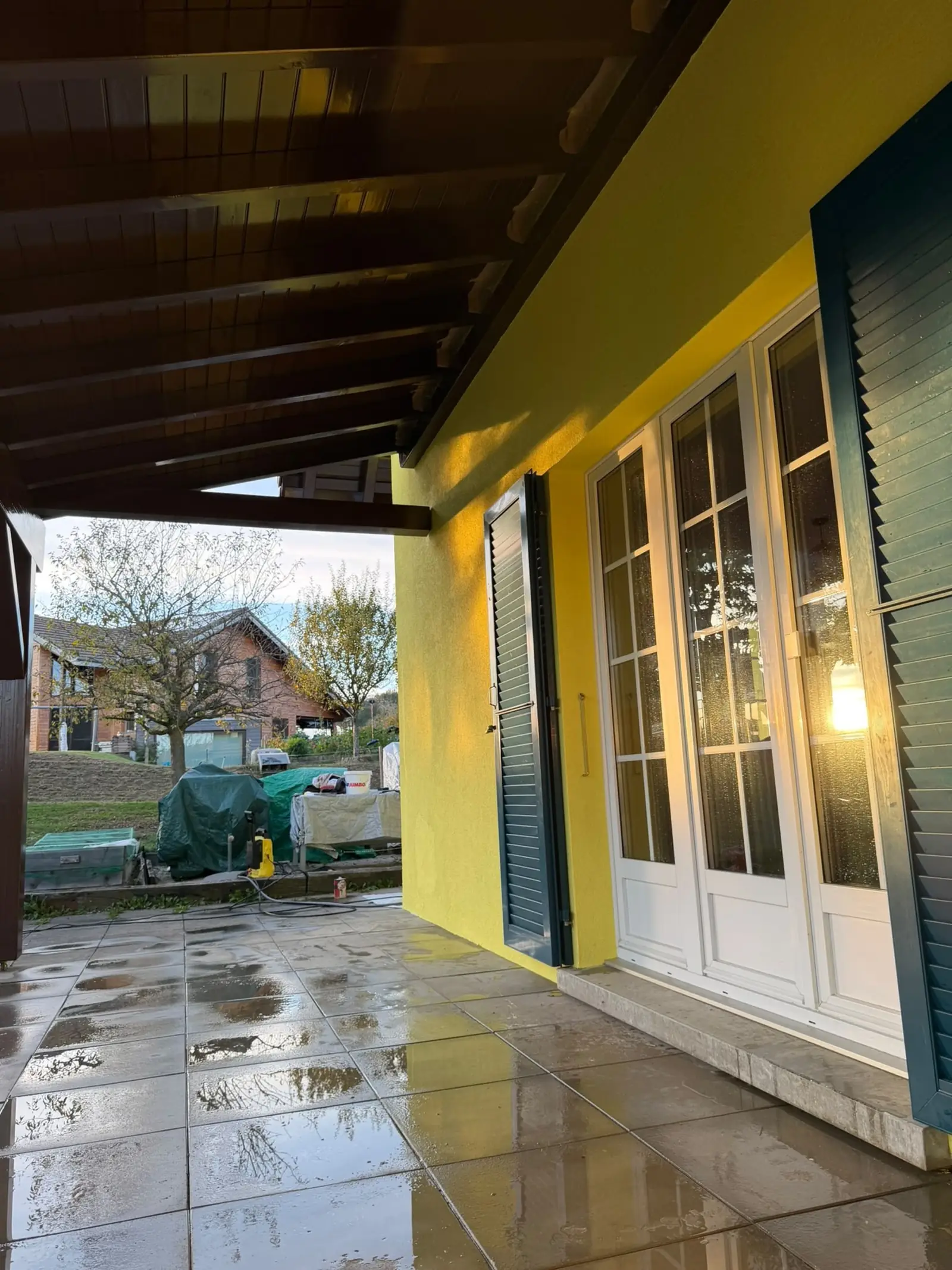 Plafond et poutres de la terrasse couverte repeints en brun, crépi jaune citron autour de la porte-fenêtre