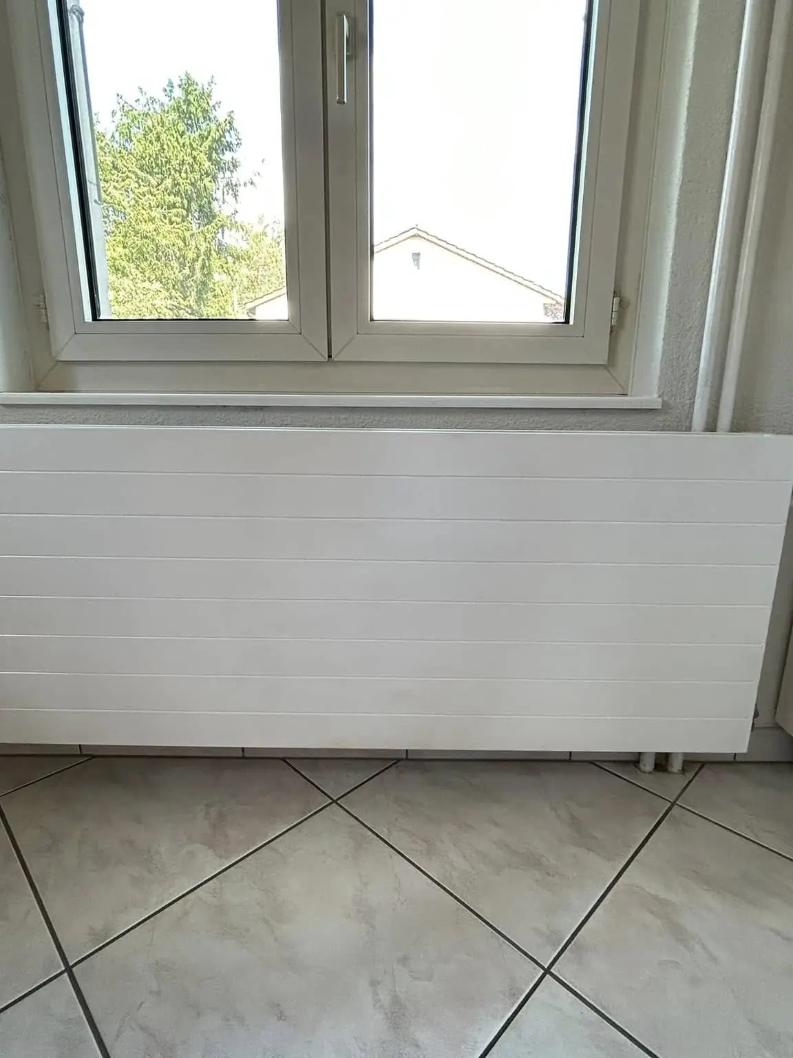 Radiateur plat repeint en blanc sous la fenêtre, mur en crépi remis en peinture autour
