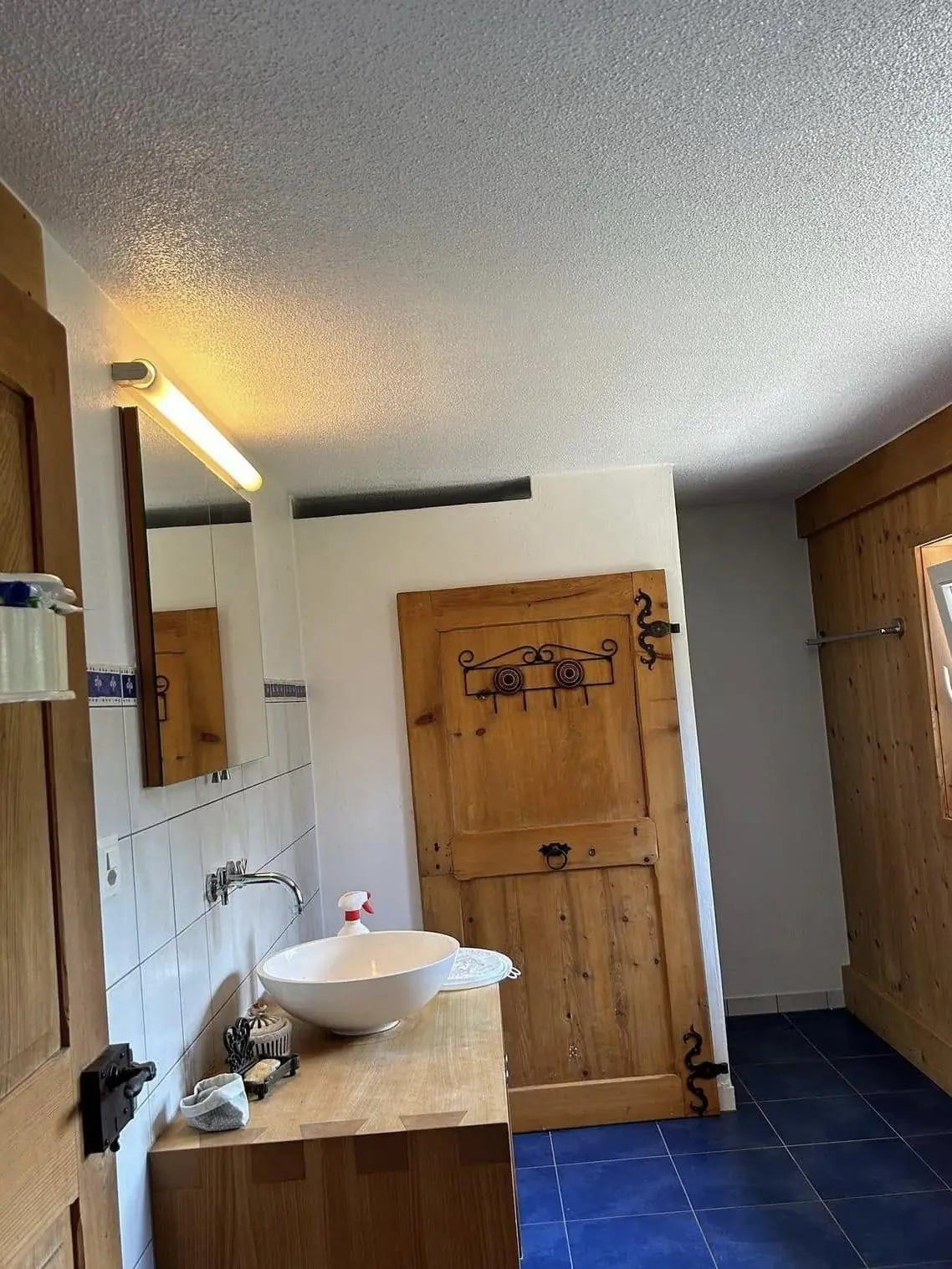 Plafond en crépi de la salle de bain peint en blanc mat, porte en vieux bois conservée